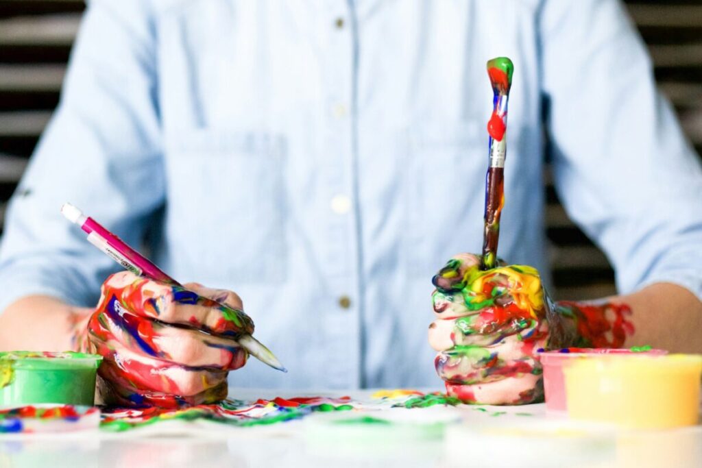 Person holding paint brushes with hands covered in paint.